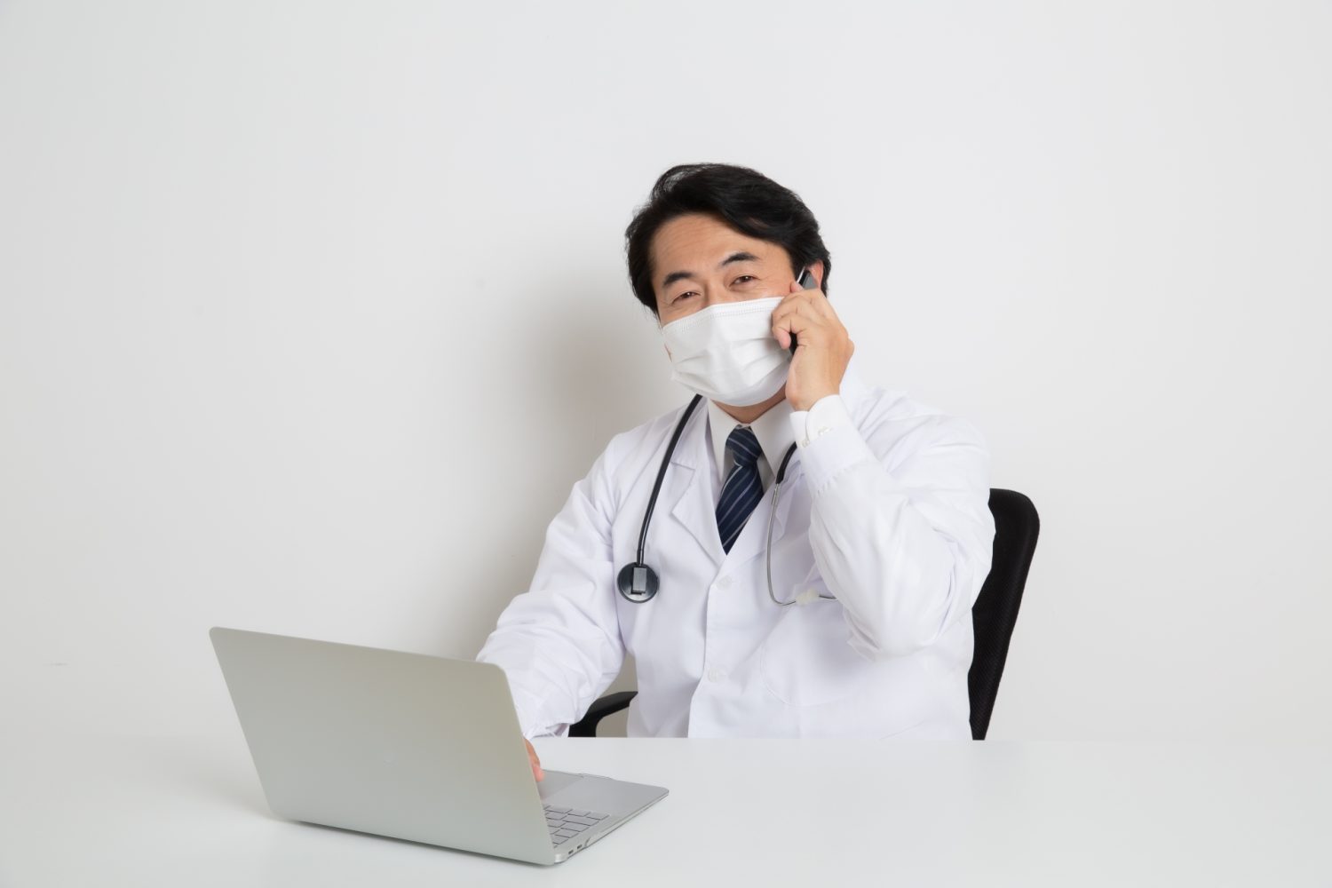 マスクをして電話をしているベテラン男性医師